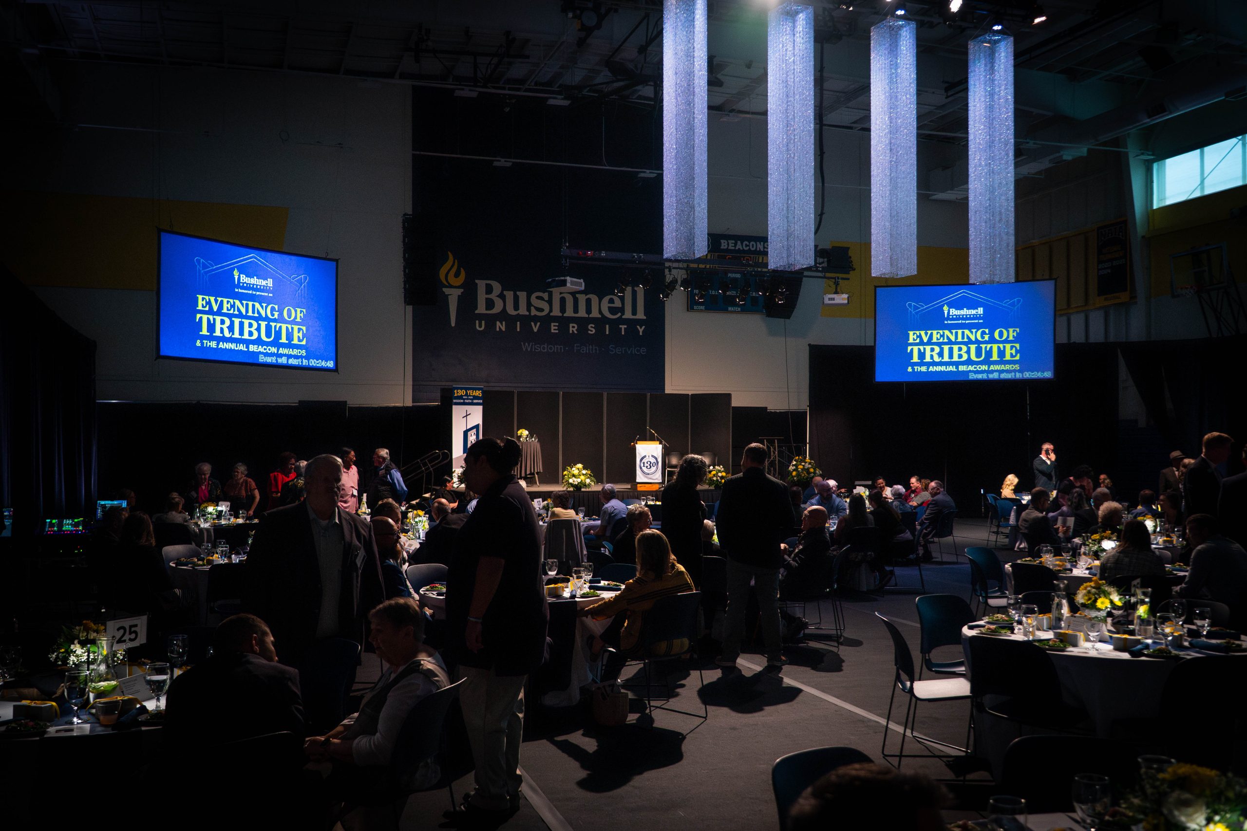 The Bushnell University basketball court transformed into a dimly lit, fancy event venue with tables and friends gathered.
