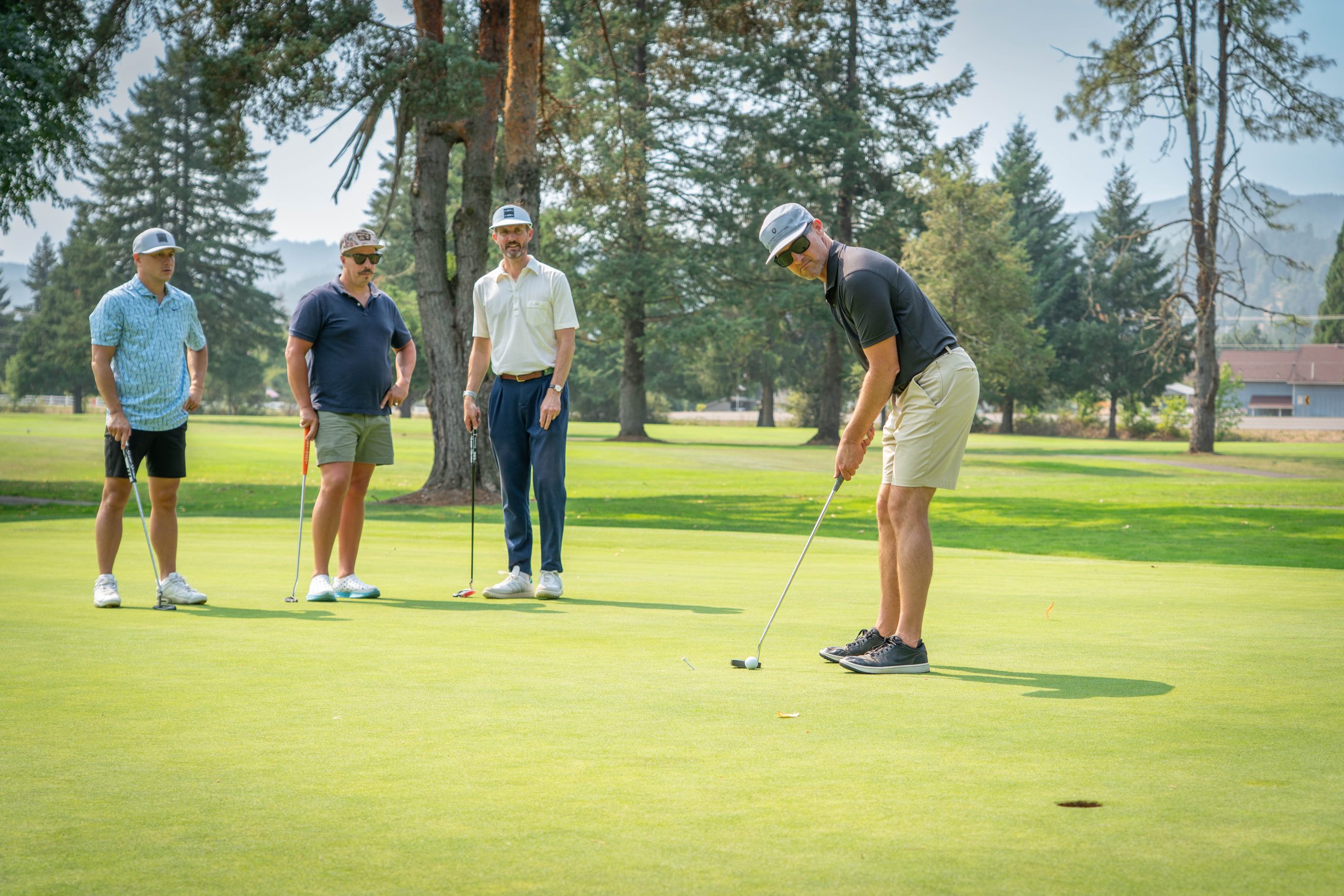 A group of golfers watch one member putt a golf ball on a bright green course during a sunny day.