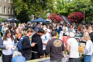 A large crowd of students check out numerous church booths hosted by staff on a sunny day during a church fair