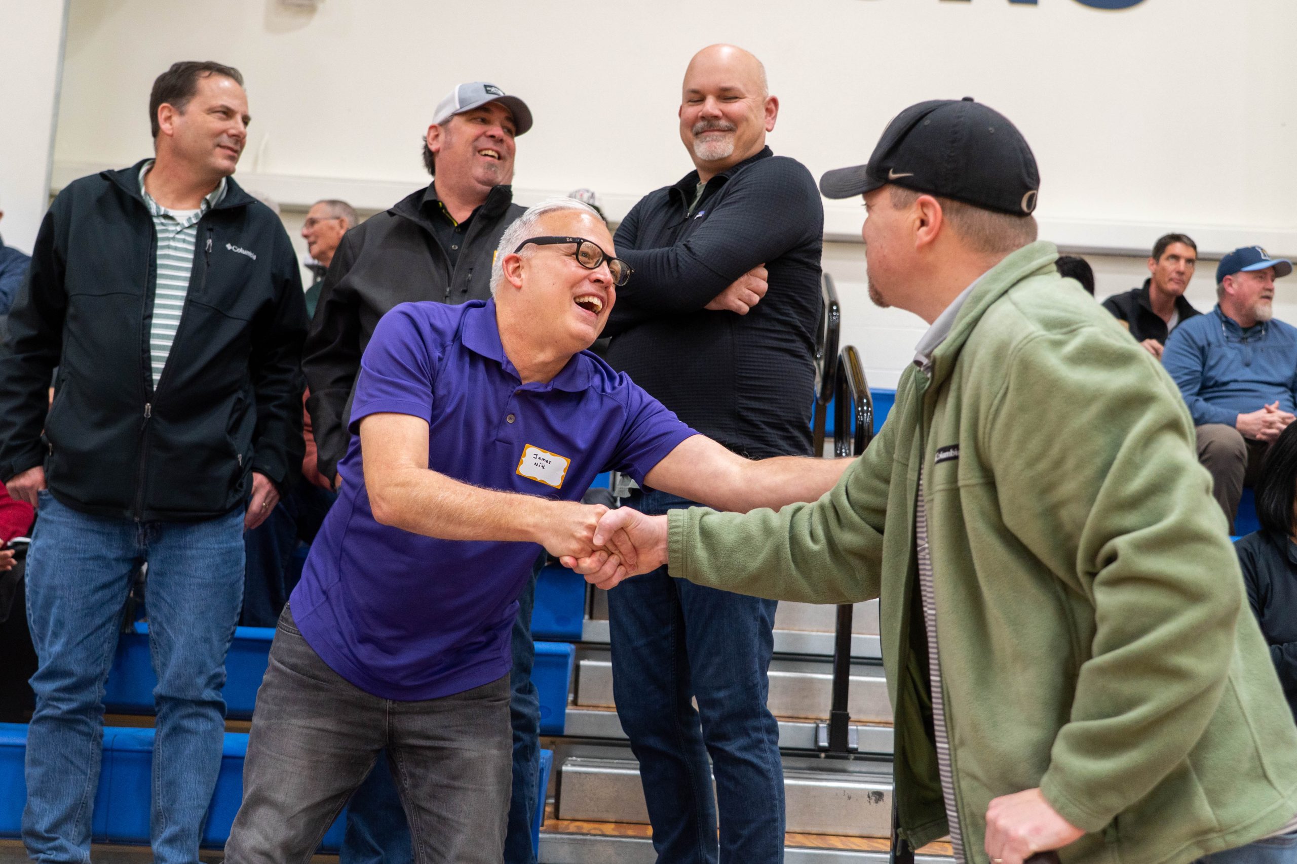 Alumni shake hands and laugh while attending a university basketball game