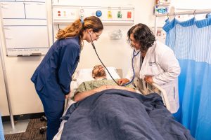 Nursing student and faculty member assess a patient in a simulated hospital room during hands-on clinical training in Bushnell University's nursing learning lab.