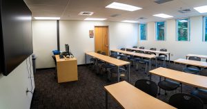 Nursing classroom with rows of tables, student seating, instructional technology, and large display screens for lecture-based learning.