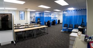 Spacious nursing simulation lab featuring patient care stations, hospital beds, instructional seating, and clinical training equipment.