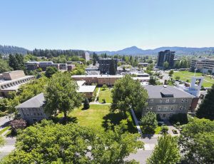Aerial view of Bushnell University campus with academic buildings, green spaces, and the Eugene hills in the background.