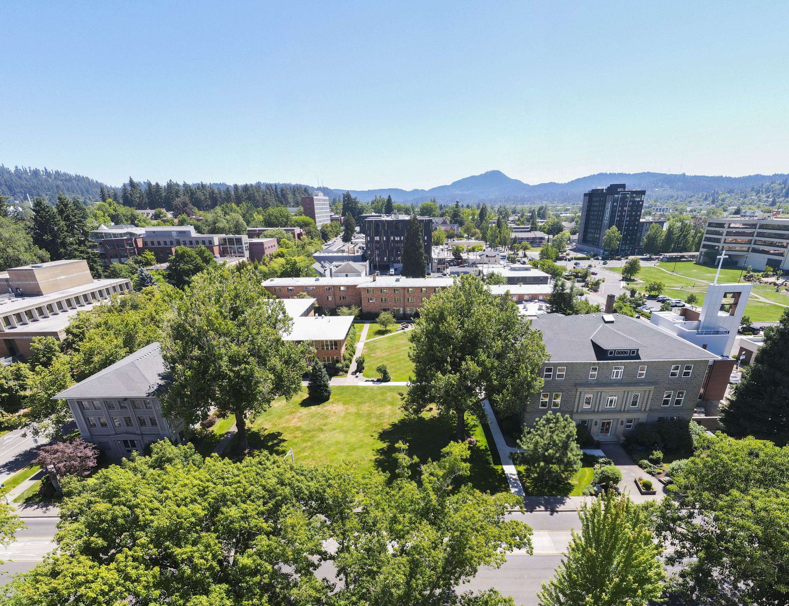 Aerial view of Bushnell University campus with academic buildings, green spaces, and the Eugene hills in the background.