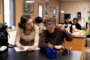 Two Bushnell University students work together in a science laboratory, analyzing a test tube and recording observations.