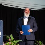 Presenter on stage holding a program during a Bushnell University awards ceremony.