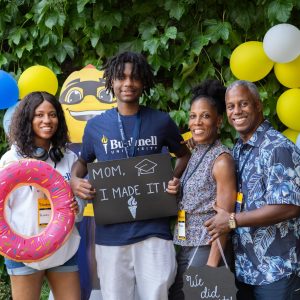 A new Bushnell University student poses with family members during orientation while holding a sign celebrating the start of the college journey.