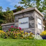 A Bushnell University monument sign surrounded by colorful flowers and landscaping at the entrance to campus in Eugene, Oregon.