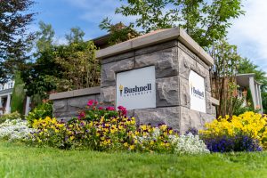 A Bushnell University monument sign surrounded by colorful flowers and landscaping at the entrance to campus in Eugene, Oregon.