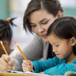 Teacher providing one-on-one reading support to an elementary student during a literacy lesson.