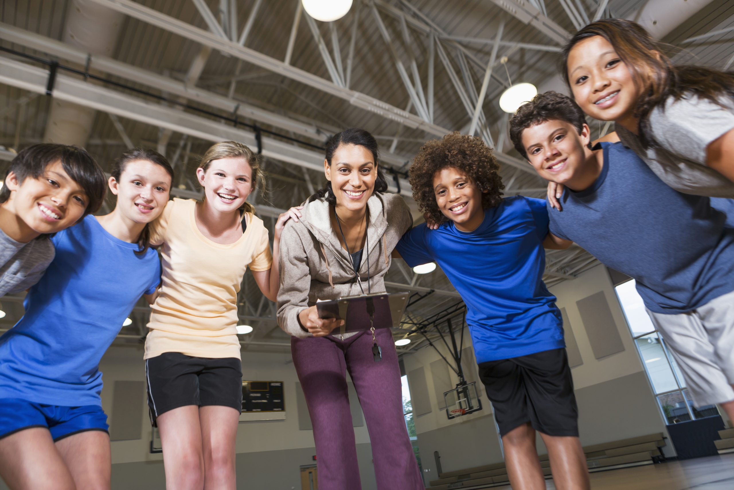 Teacher leading a group of elementary students during a physical education lesson in a school gym.