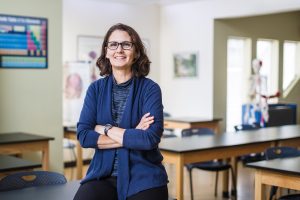 Female psych professor with glasses crossing her arms in a blue cardigan.