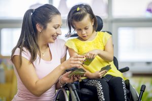 Teacher working one-on-one with a young student using a wheelchair during a classroom learning activity.