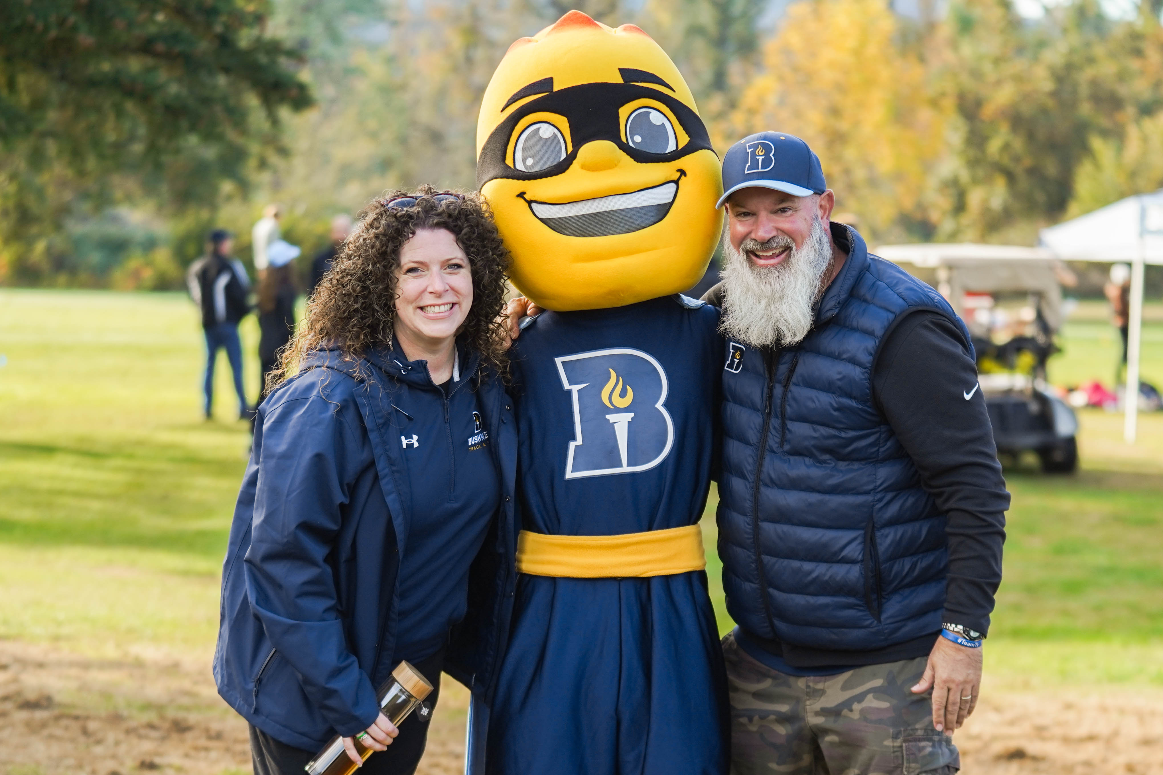 Athletic Directors Corey and Sarah smiling with university mascot Iggy Beacon during a Cross Country event.