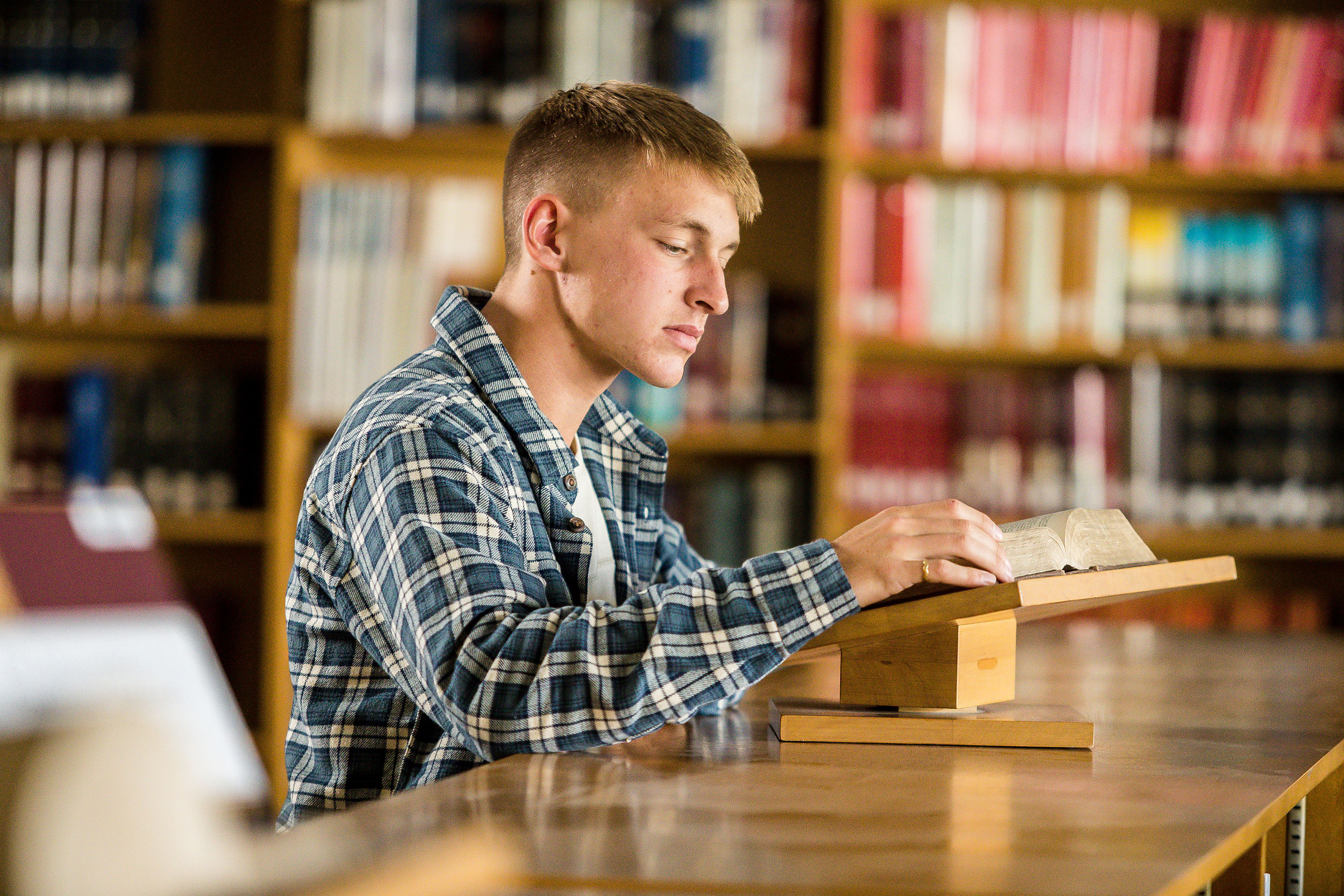 A bible, theology, and ministry student reads scripture from a bible in a library.
