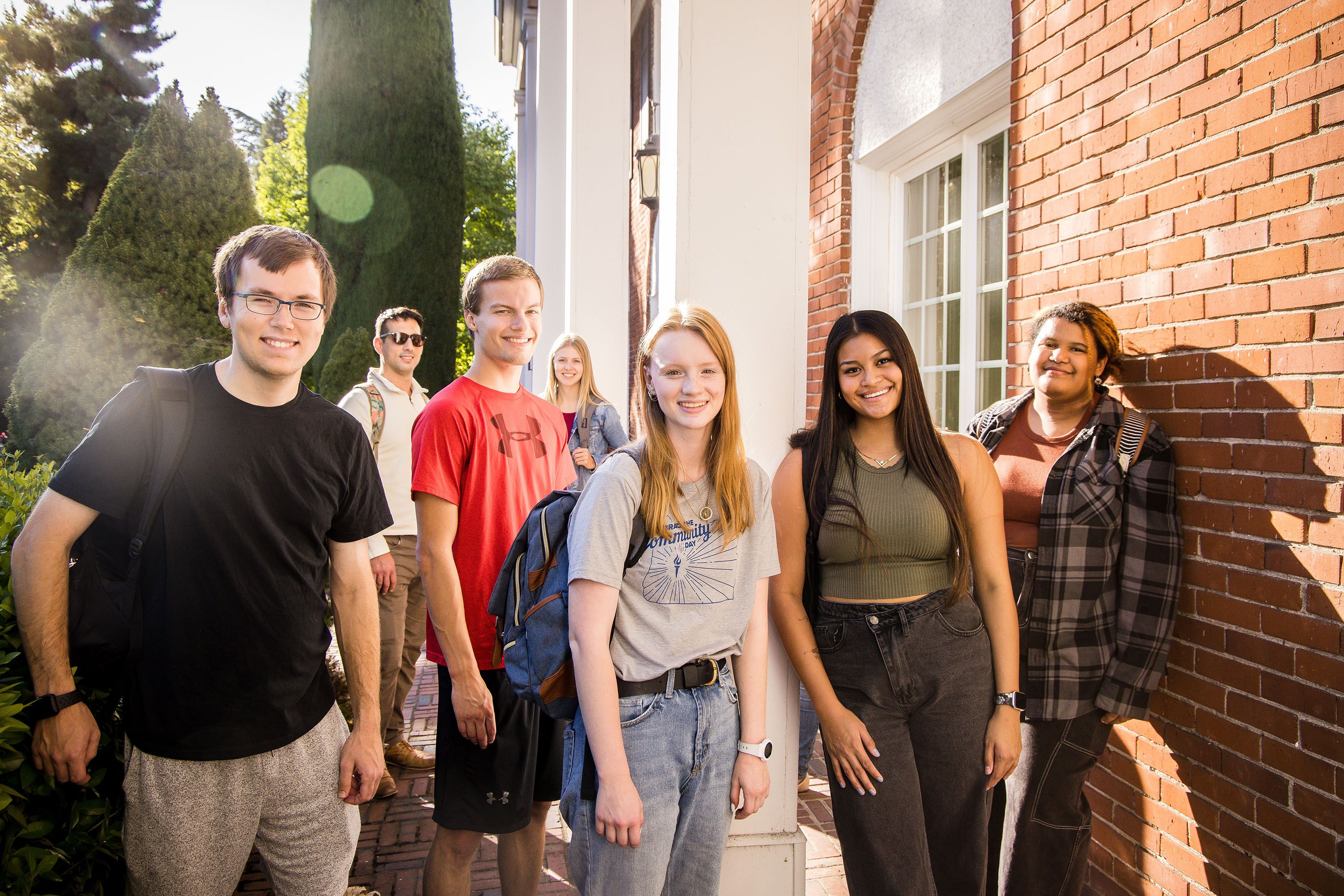A group of students posing together next to a brick building during golden hour.