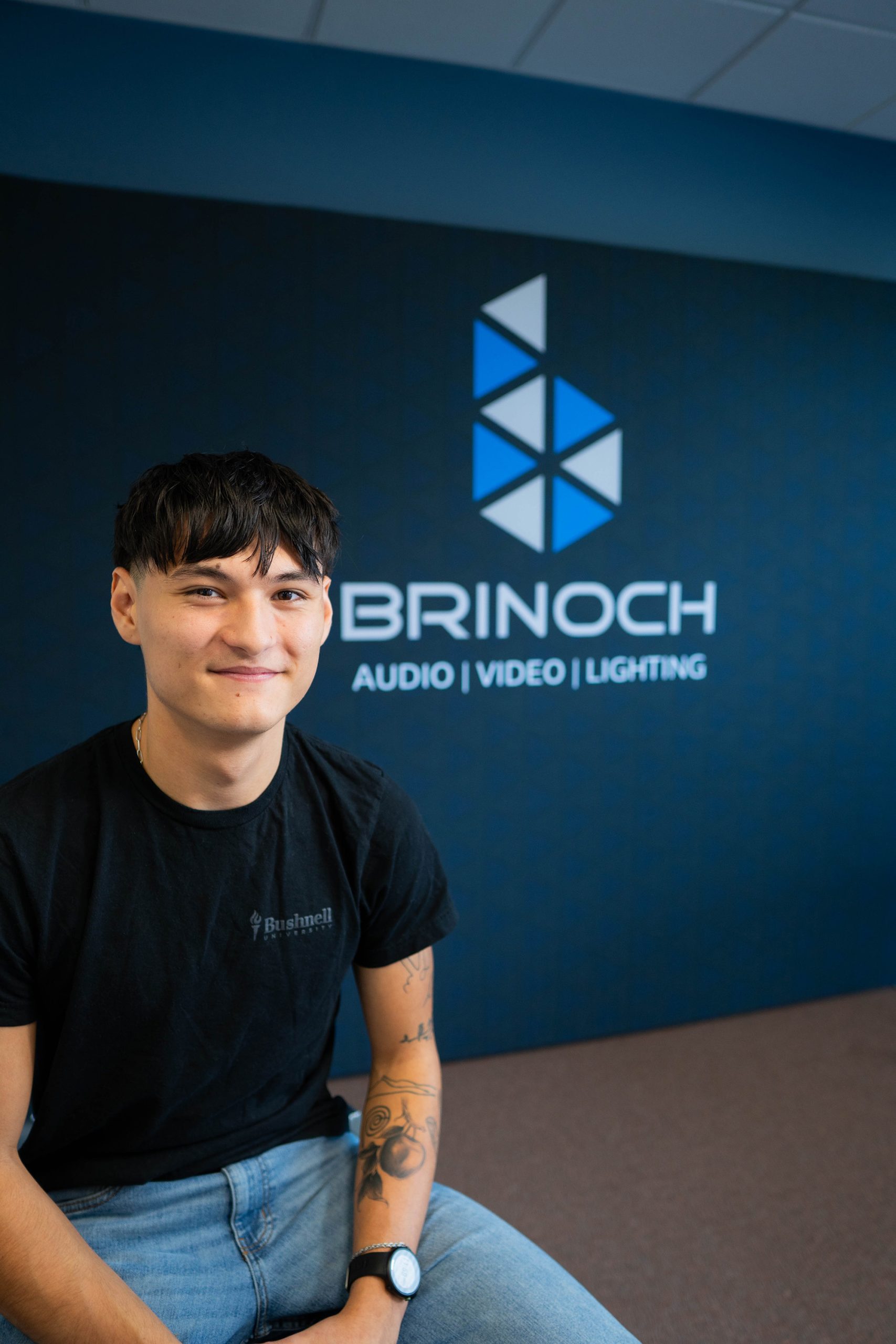 Student intern at local Audio, Video, and Lighting company posing with logo in the background.