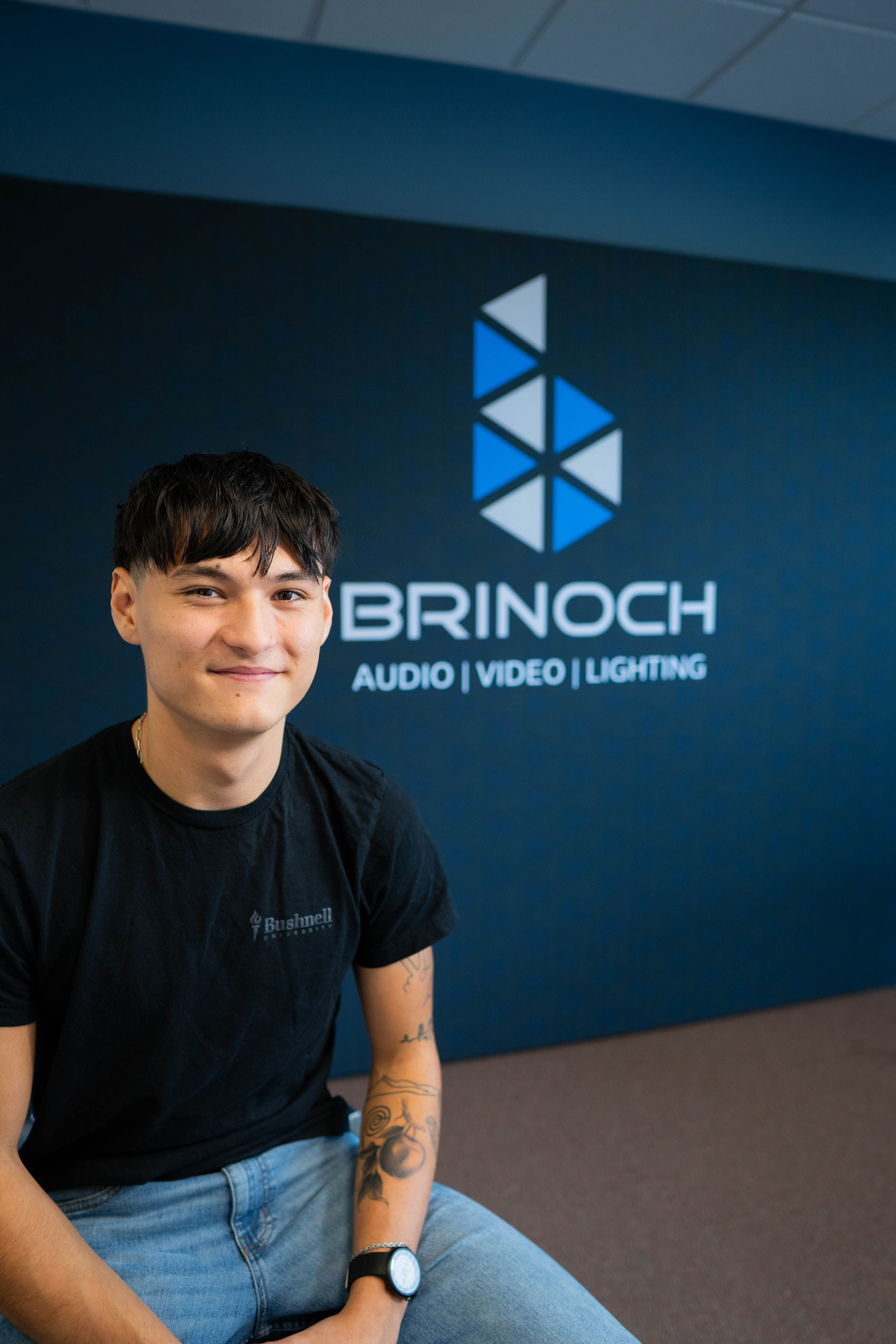 Student intern at local Audio, Video, and Lighting company posing with logo in the background.