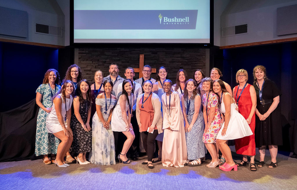 Bushnell University ABSN graduates and faculty pose together on stage during the nursing pinning ceremony.