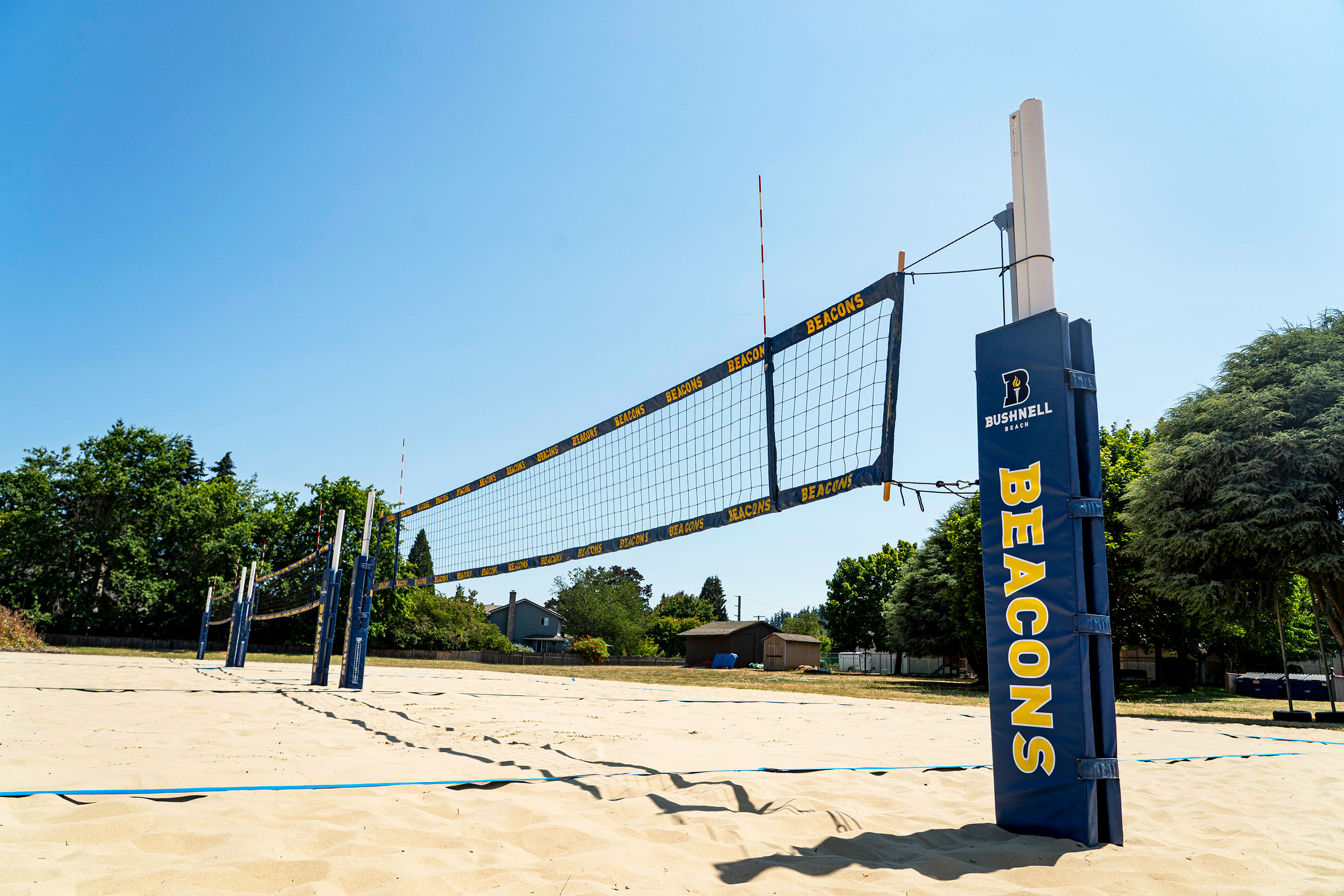 Sandy volleyball courts next to trees with three blue nets with Beacons written in yellow.