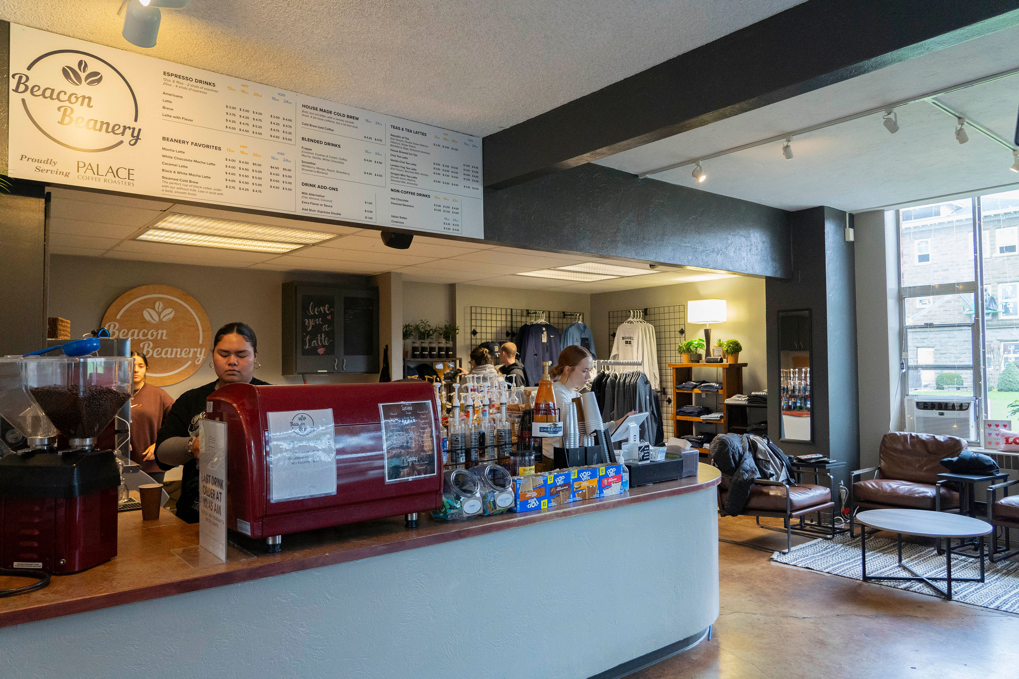 Bushnell Beacon Beanery photo showing long counter with coffee makers, snacks, and Bushnell gear shop as student baristas work.