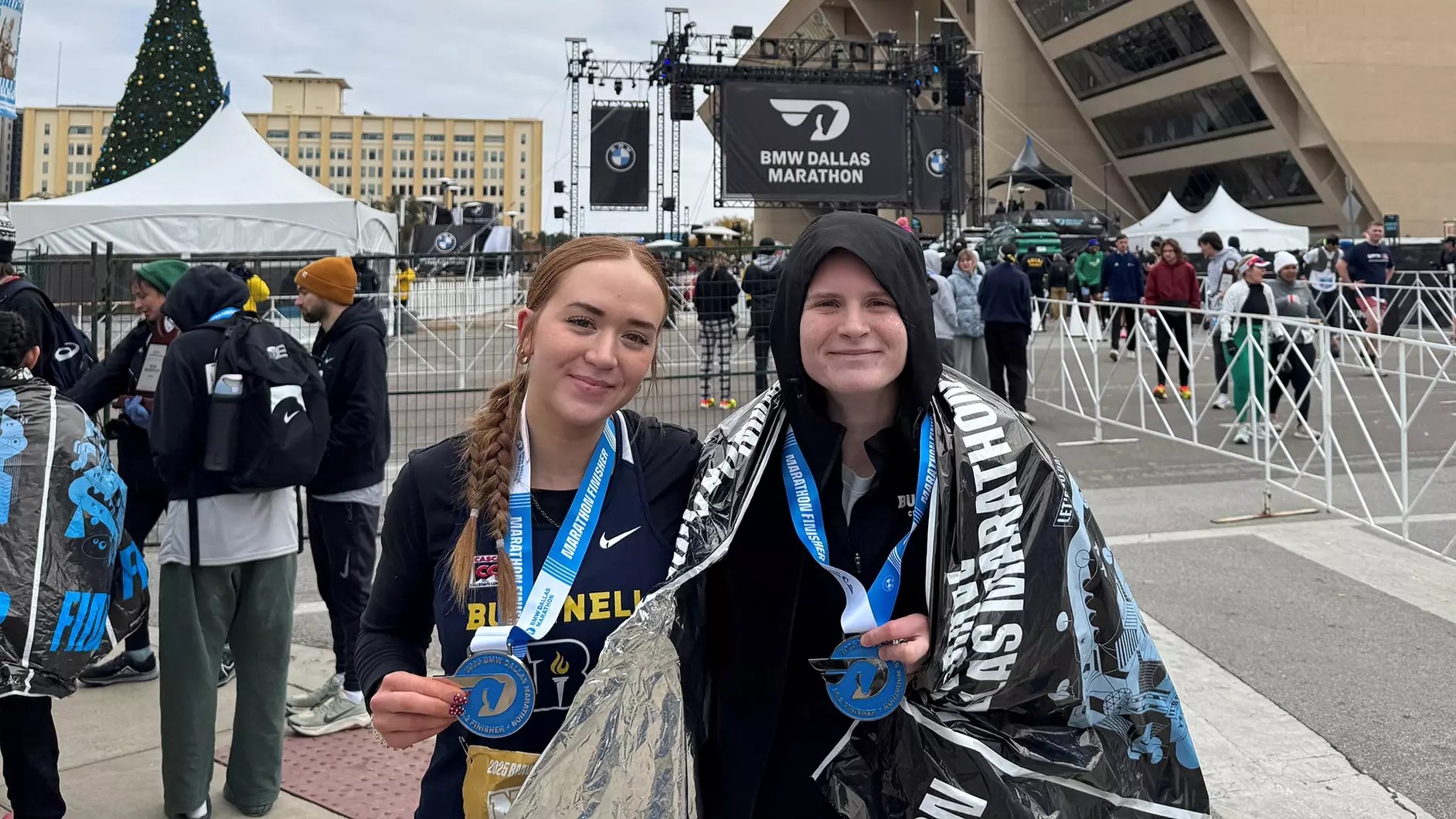 Two Bushnell University cross country students display their finisher medals after completing the BMW Dallas Marathon.