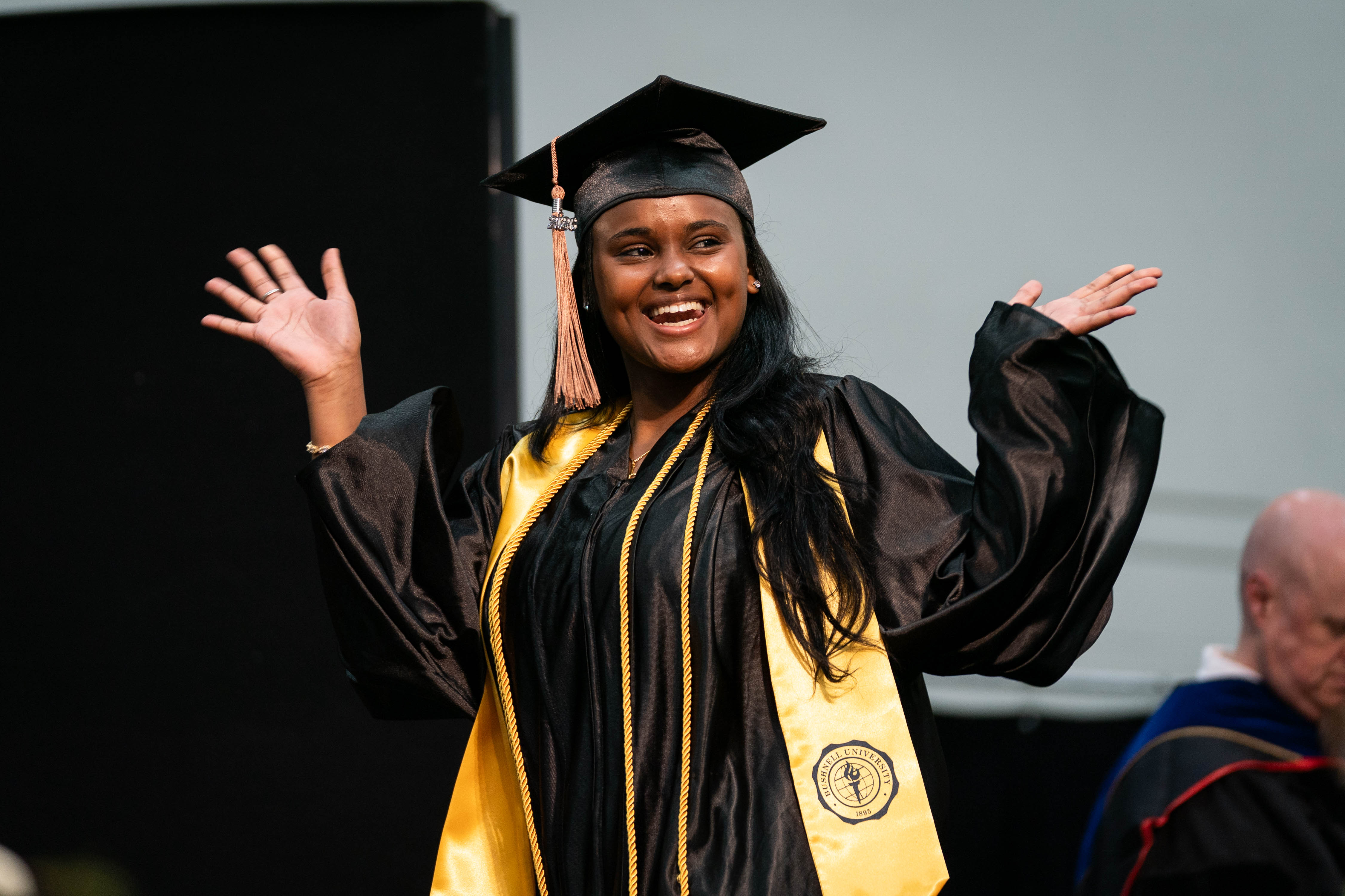 A Bushnell University student celebrates and waves to the crowd as they walk to receive their diploma.