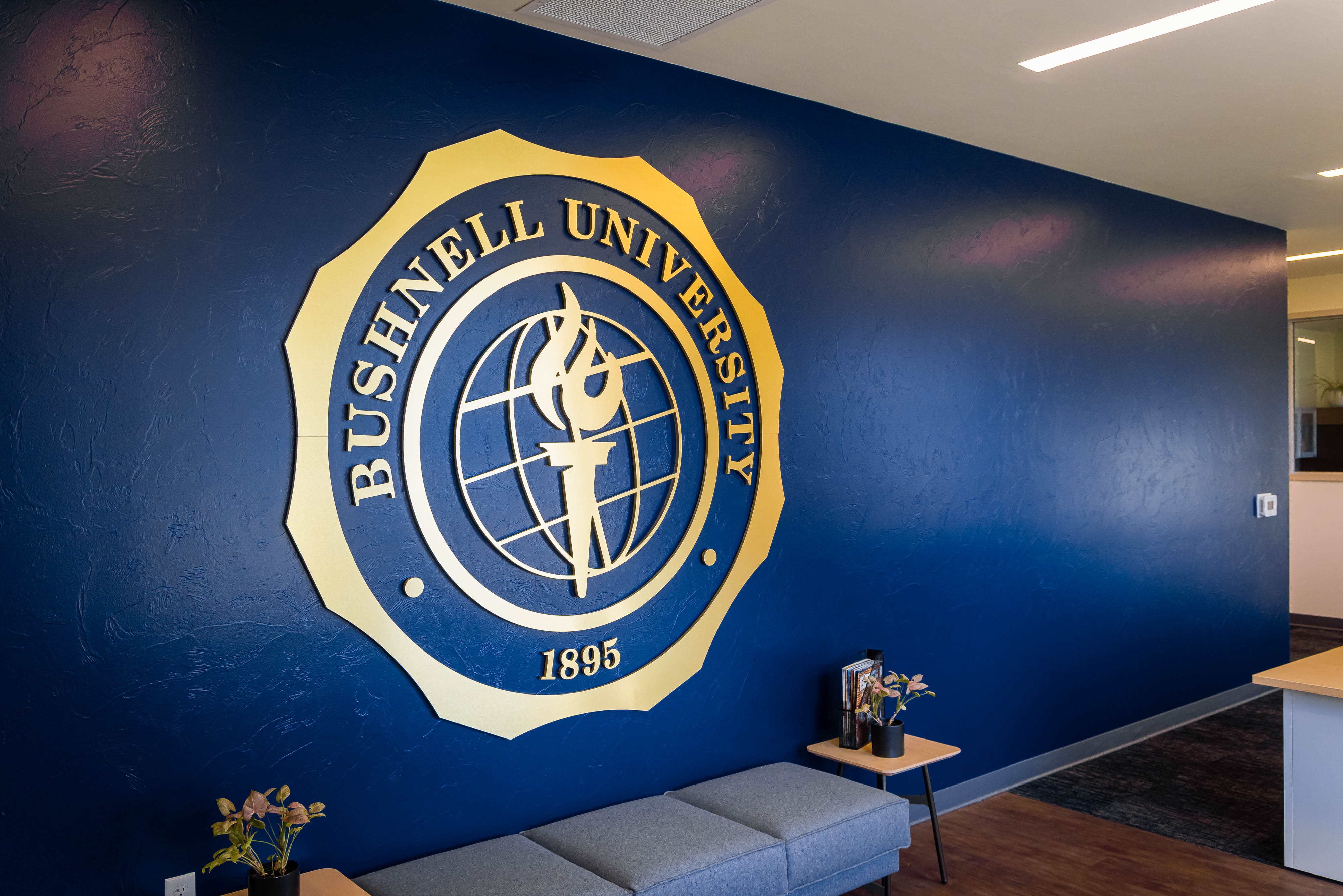 A massive golden Bushnell President's Seal display on a long blue wall in the Office of the President.