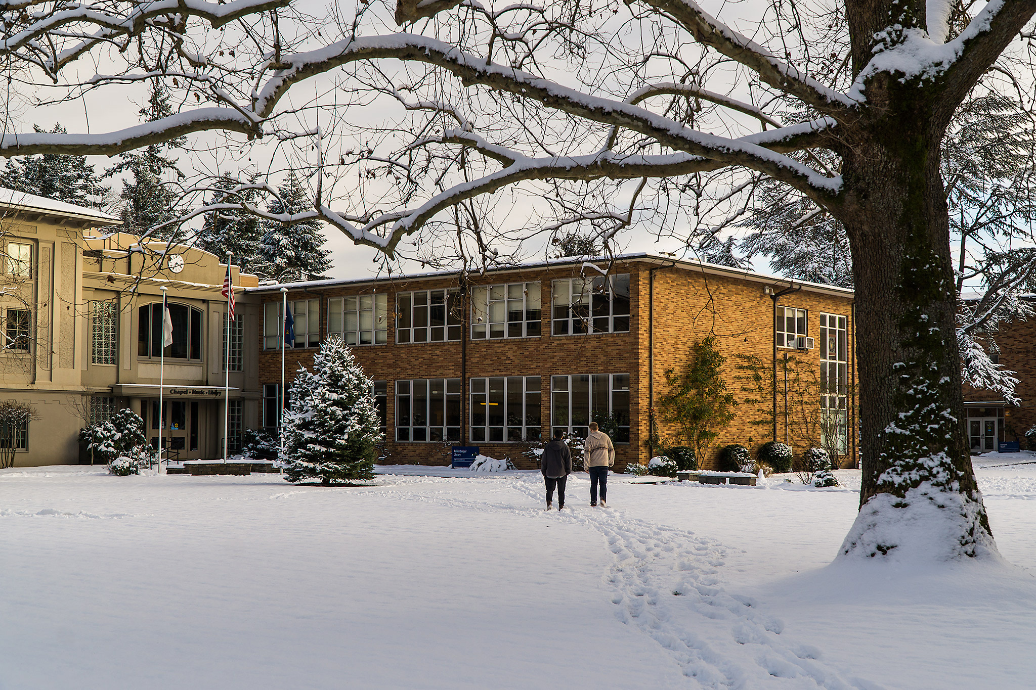 Bushnell snow day featuring brick library building and quad area covered in snow with two students walking through.