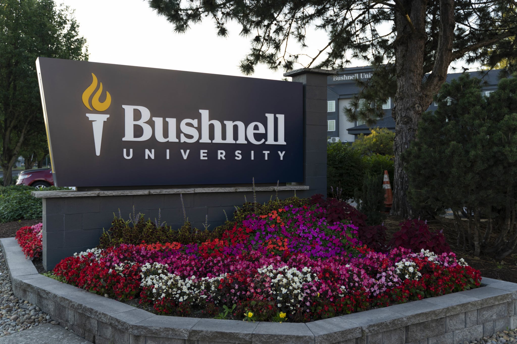 Bushnell University entrance sign surrounded by colorful flowers and landscaped gardens at the Eugene, Oregon campus.