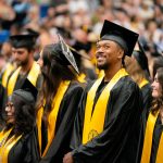Bushnell University graduates celebrate during commencement ceremony wearing caps, gowns, and gold stoles.