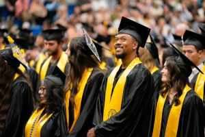 Bushnell University graduates celebrate during commencement ceremony wearing caps, gowns, and gold stoles.
