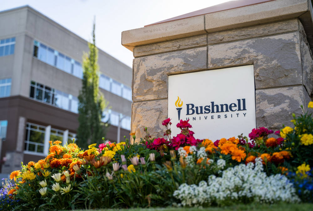 Bushnell University sign on campus with flowers in the foreground