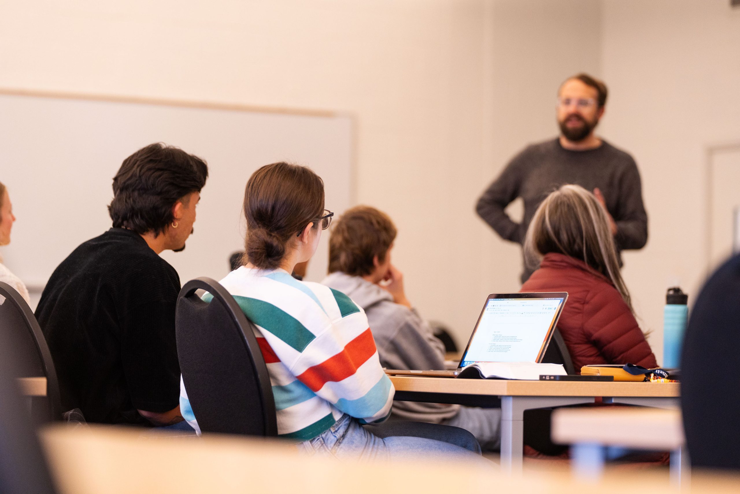A classroom setting with students focussed on a teacher at the front of class.