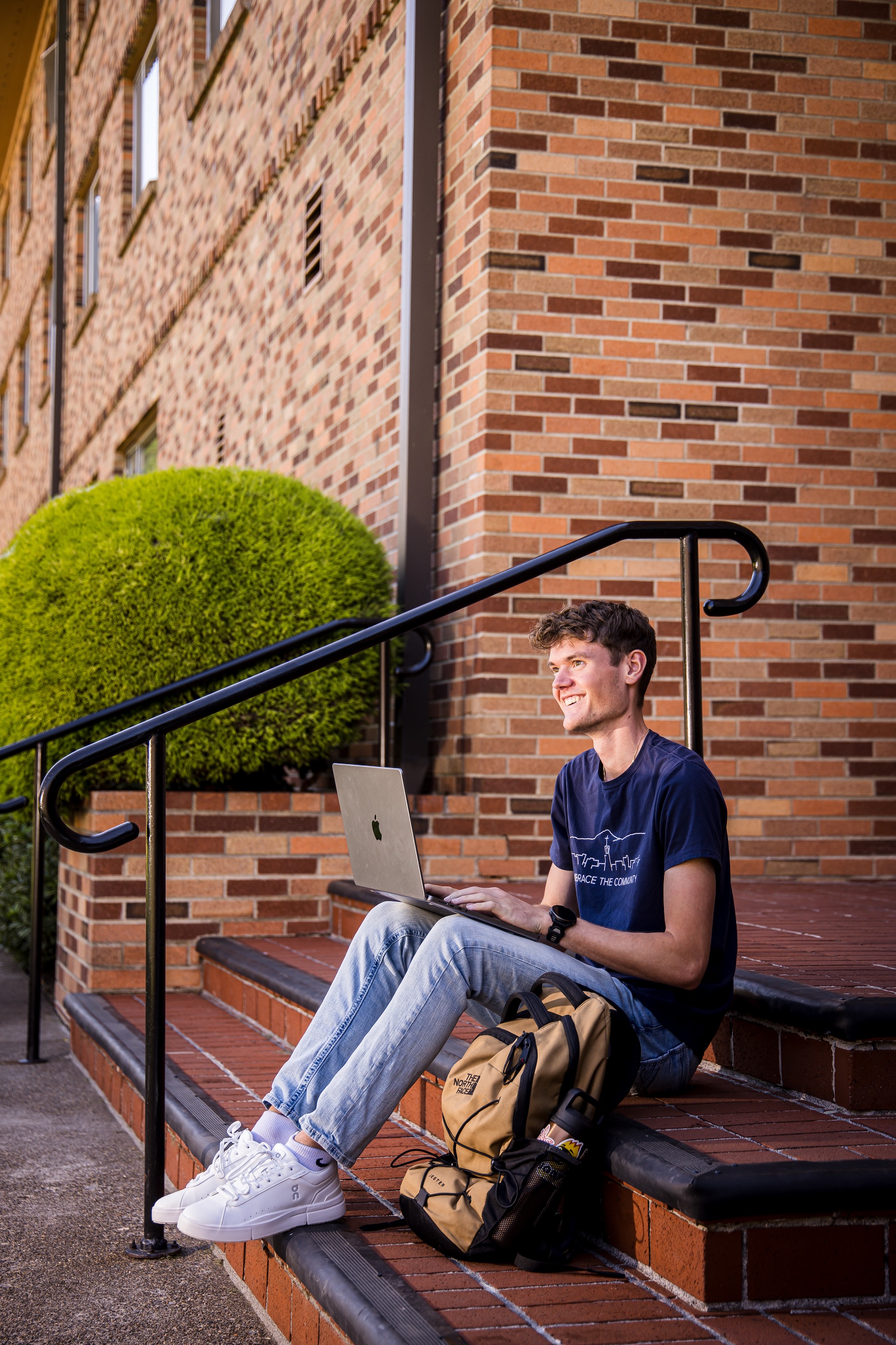 Bushnell University student studying on a laptop outside on campus steps.