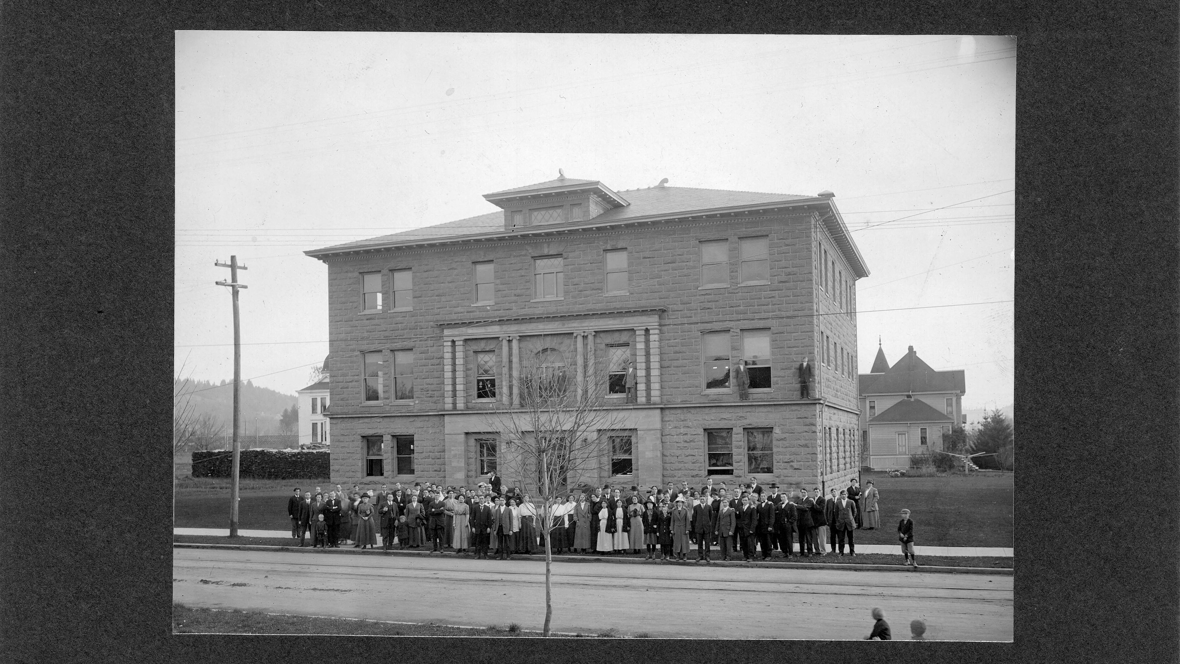Historic black and white photo of Goodrich Hall admin building made of stone with large crowd from 1912.