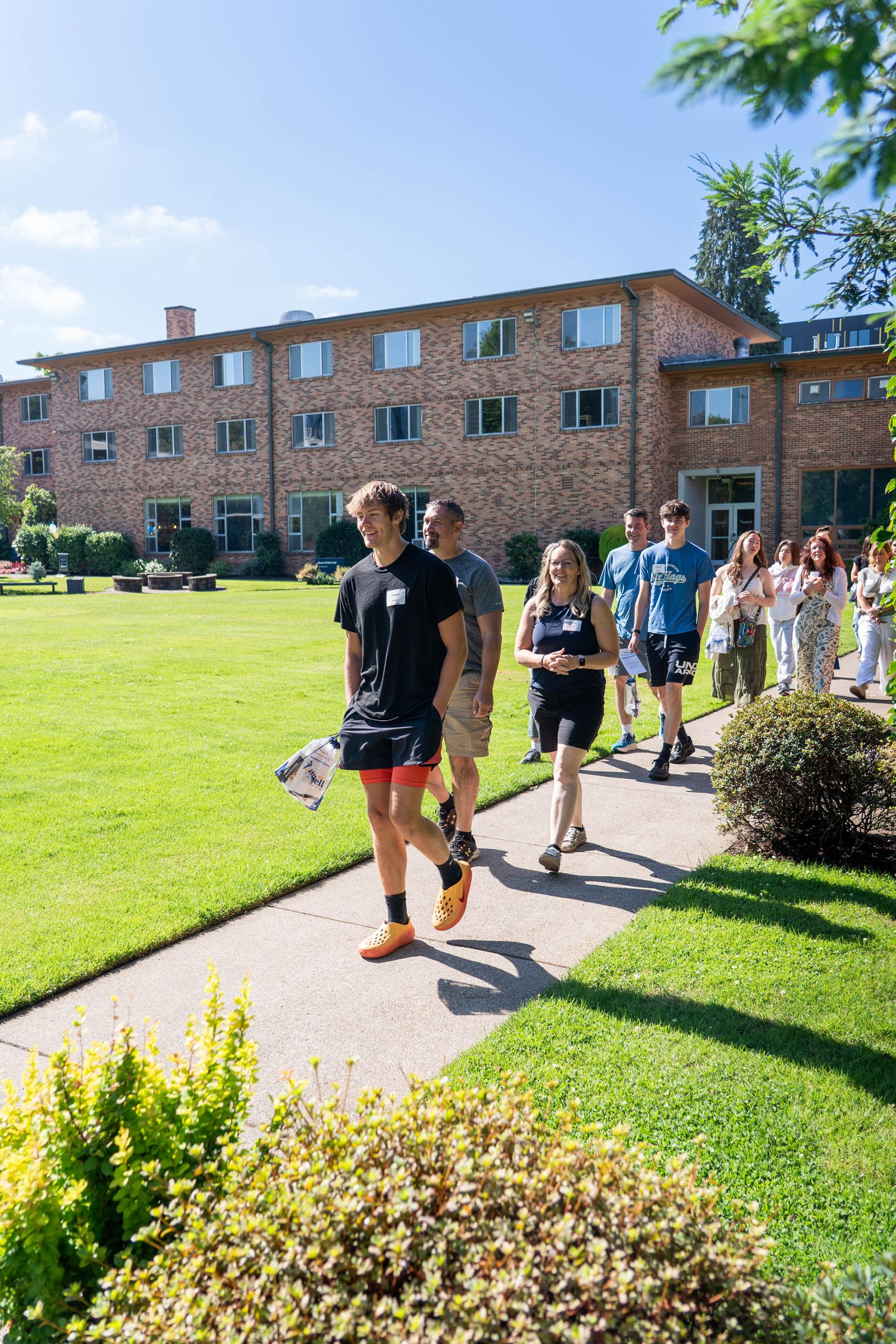 Students and families on Bushnell Preview Day tour campus in the sun with a brick dorm building in the background.