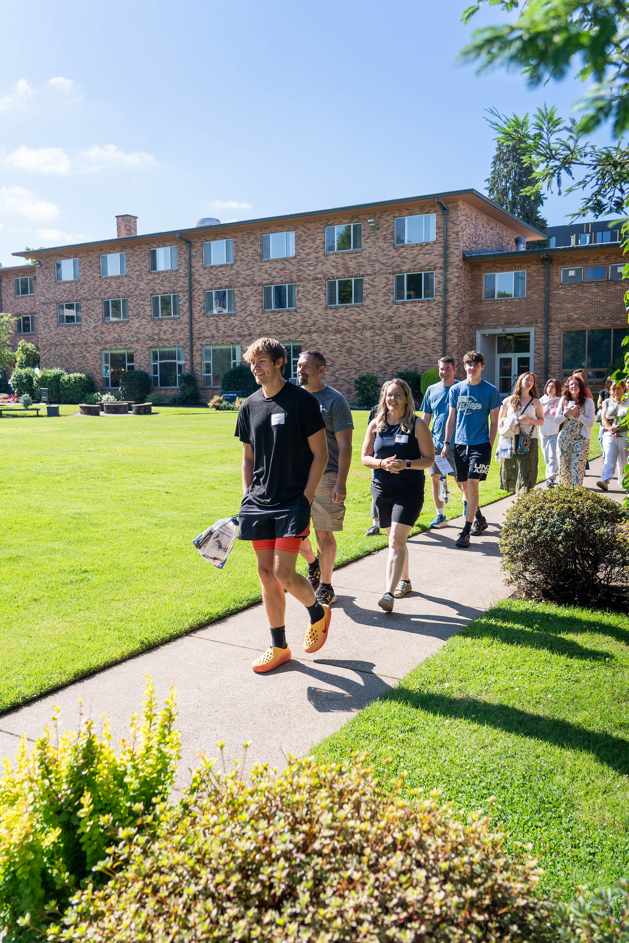 Students and families on Bushnell Preview Day tour campus in the sun with a brick dorm building in the background.