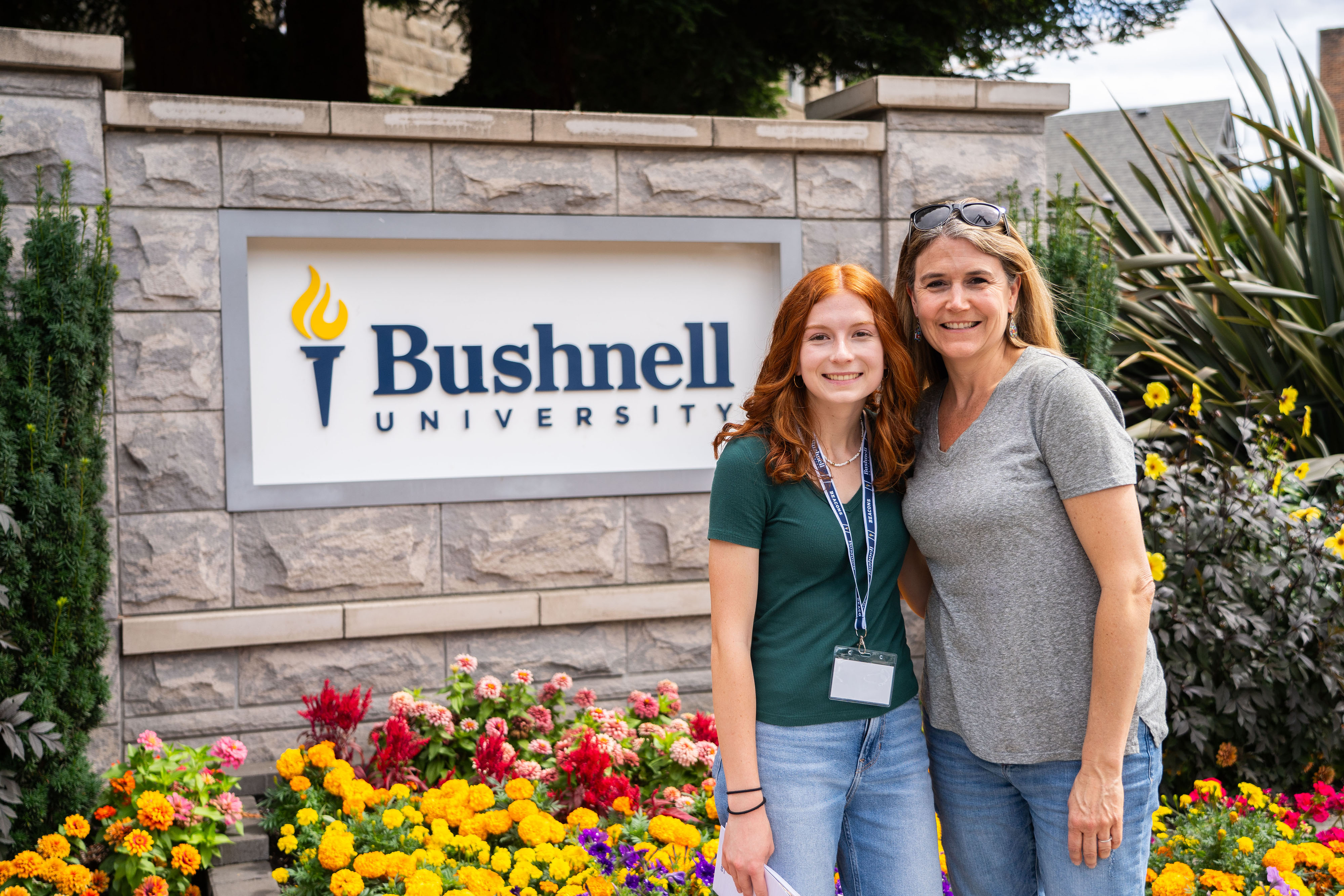 A photo of a family visit on Bushnell University campus in front of the university monument sign with flowers.