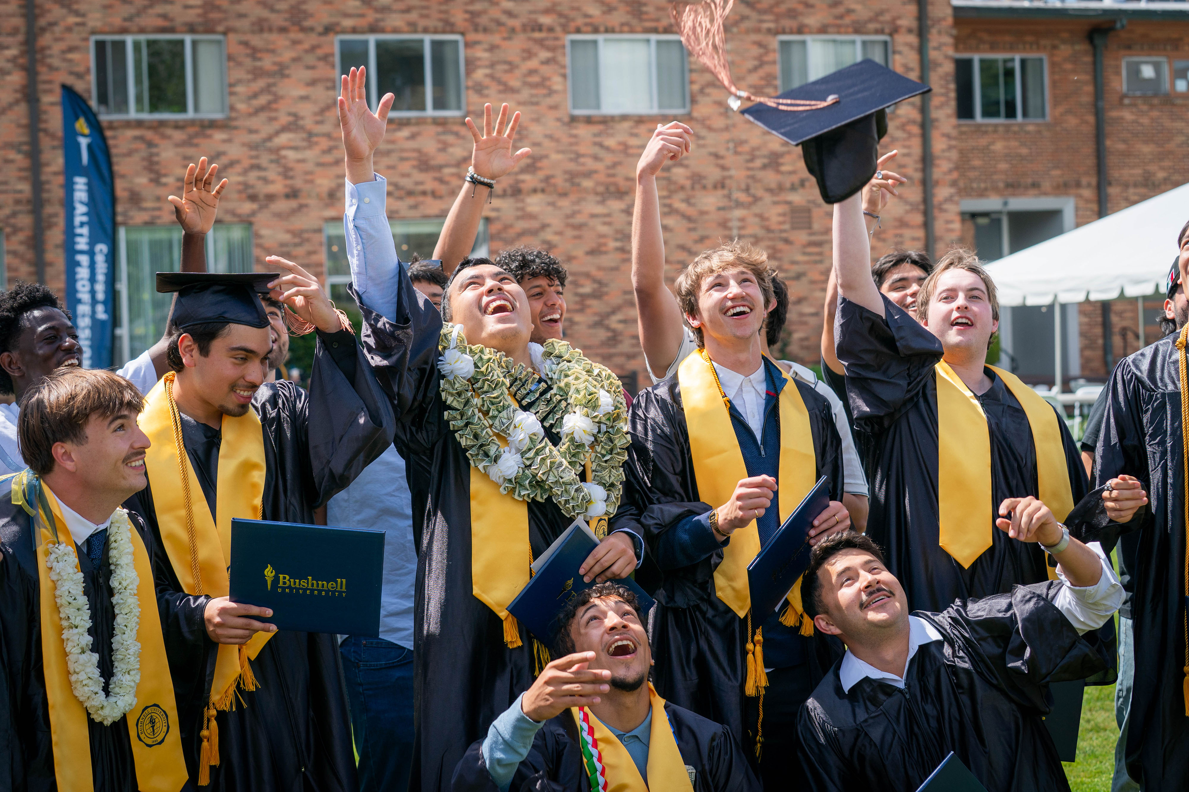 Graduated students in gowns and gold stoles toss their caps up in celebration.