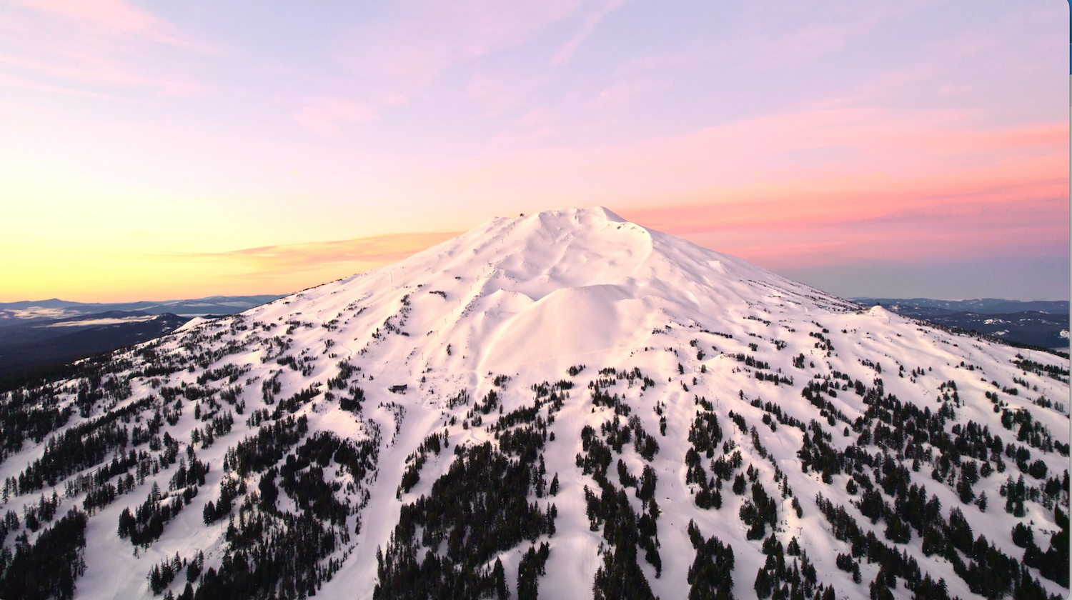 Snow-covered Mount Bachelor in Central Oregon at sunrise beneath a colorful pink and orange sky.