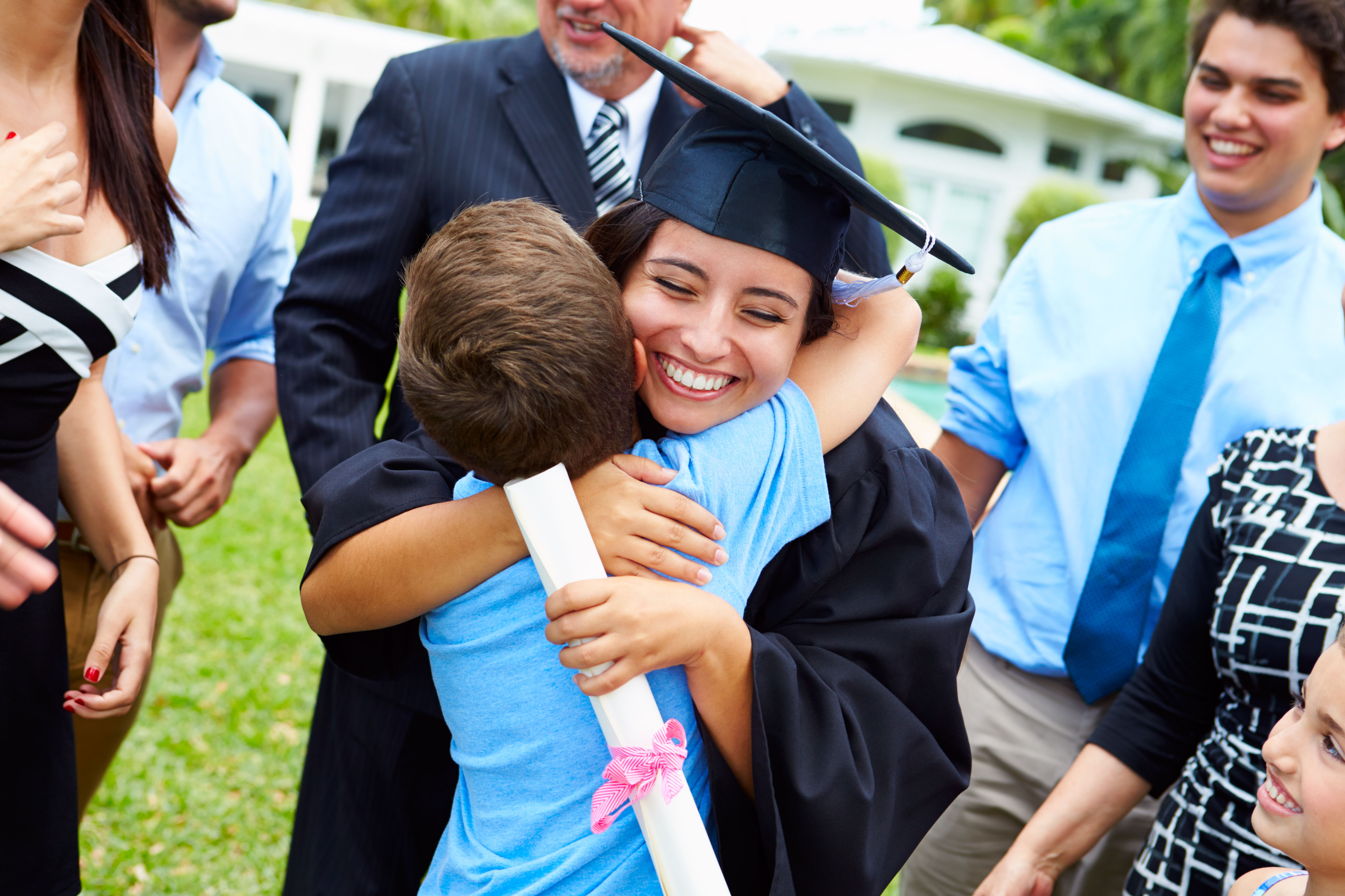 A parent in graduation gown and cap embraces a child while being surrounded by family.