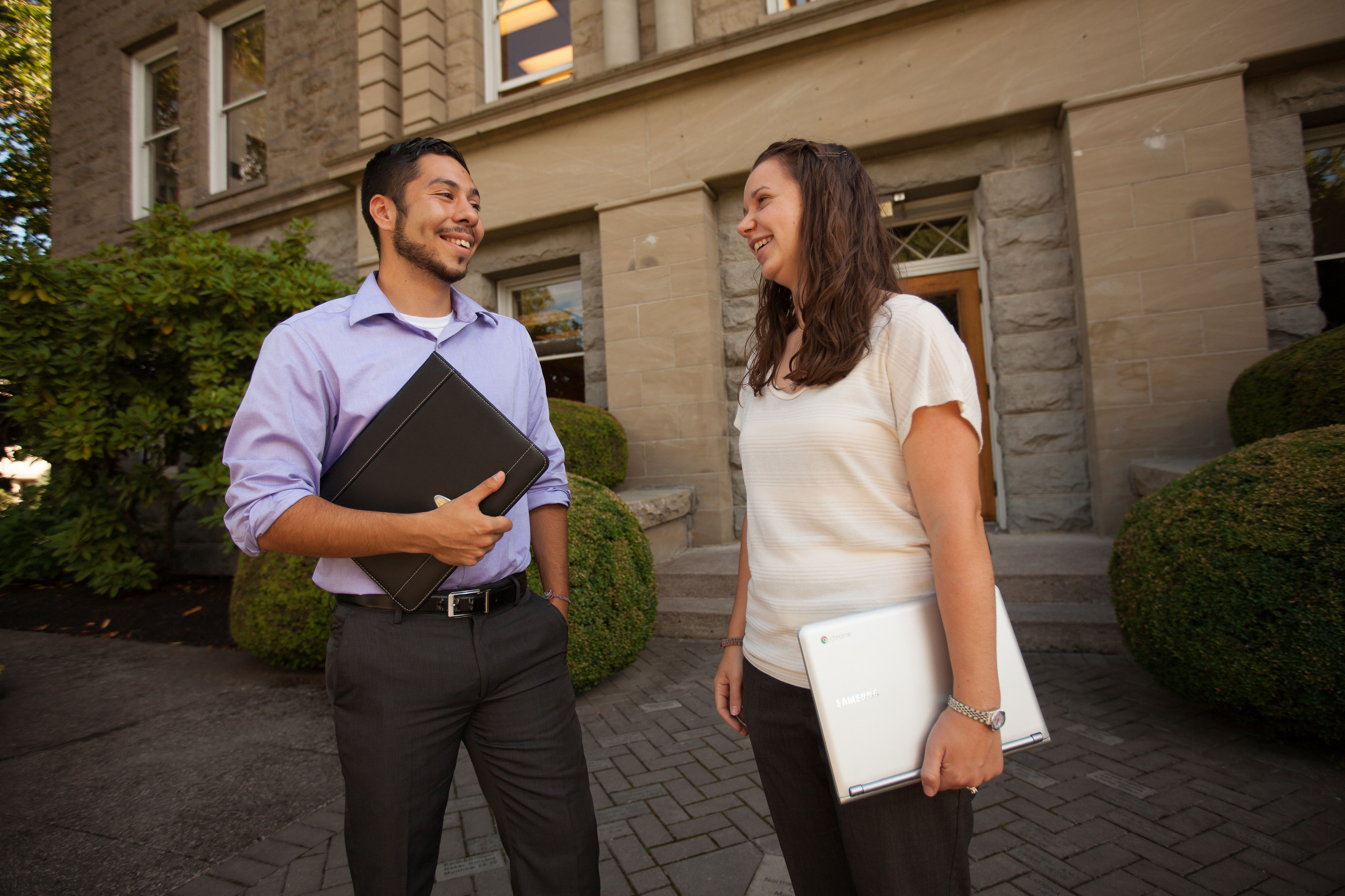 Professionally dressed graduate students from the business program chat outside an academic building.
