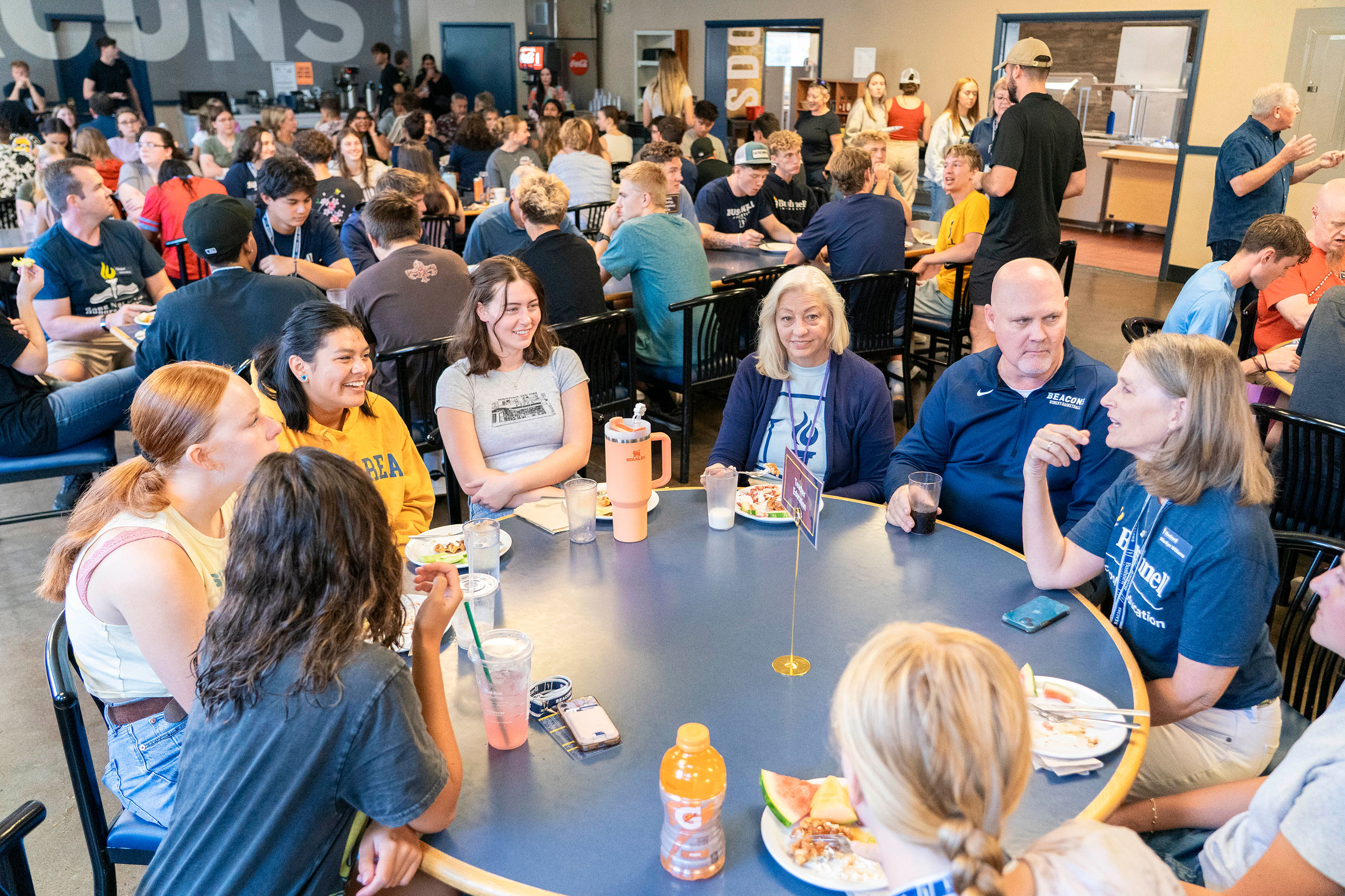 Professors and new students chatting while sitting at a round table in the Bushnell University cafeteria during an Orientation event.