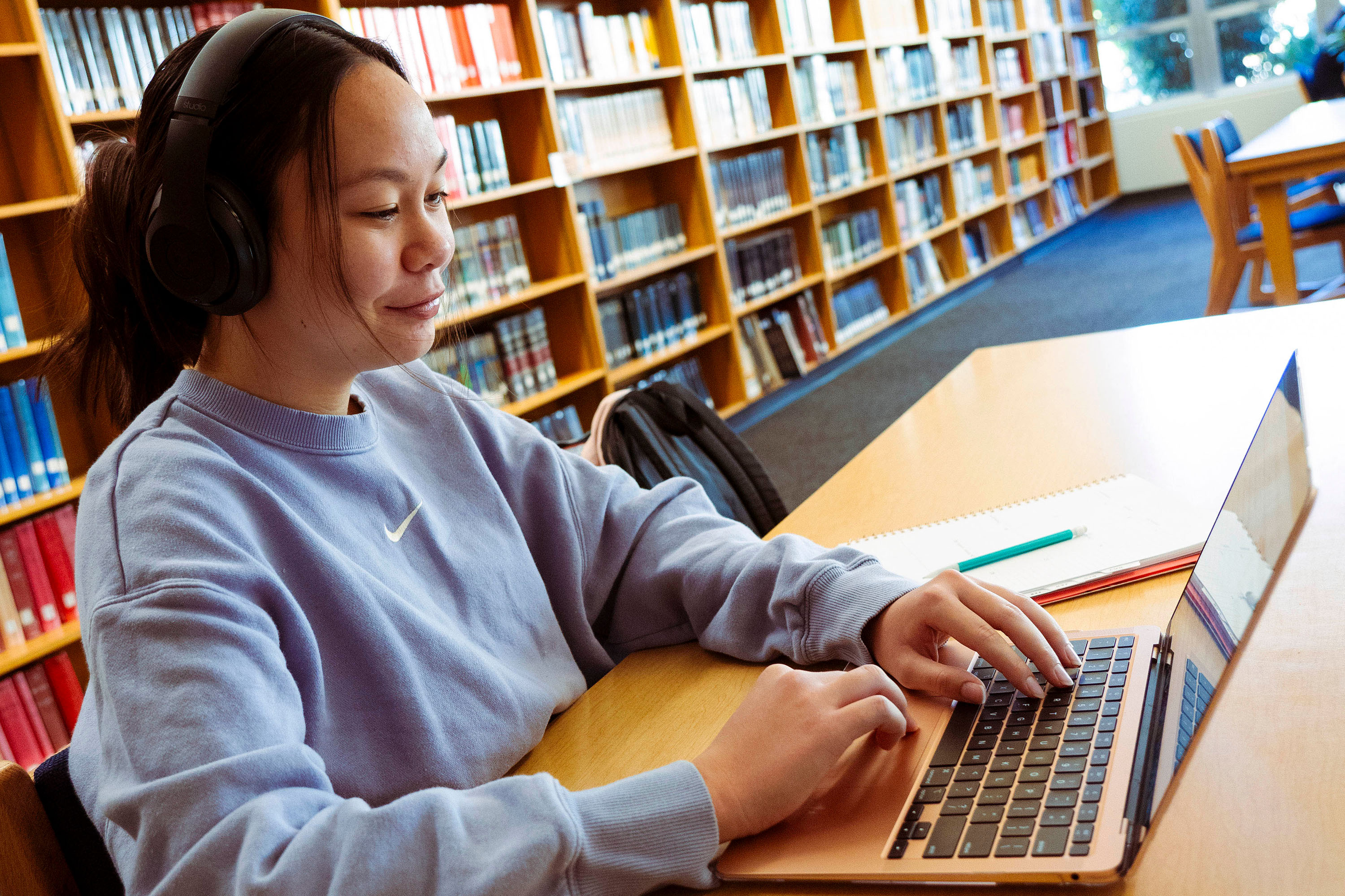 Transfer student in sweatshirt and headphones on their laptop smiling.