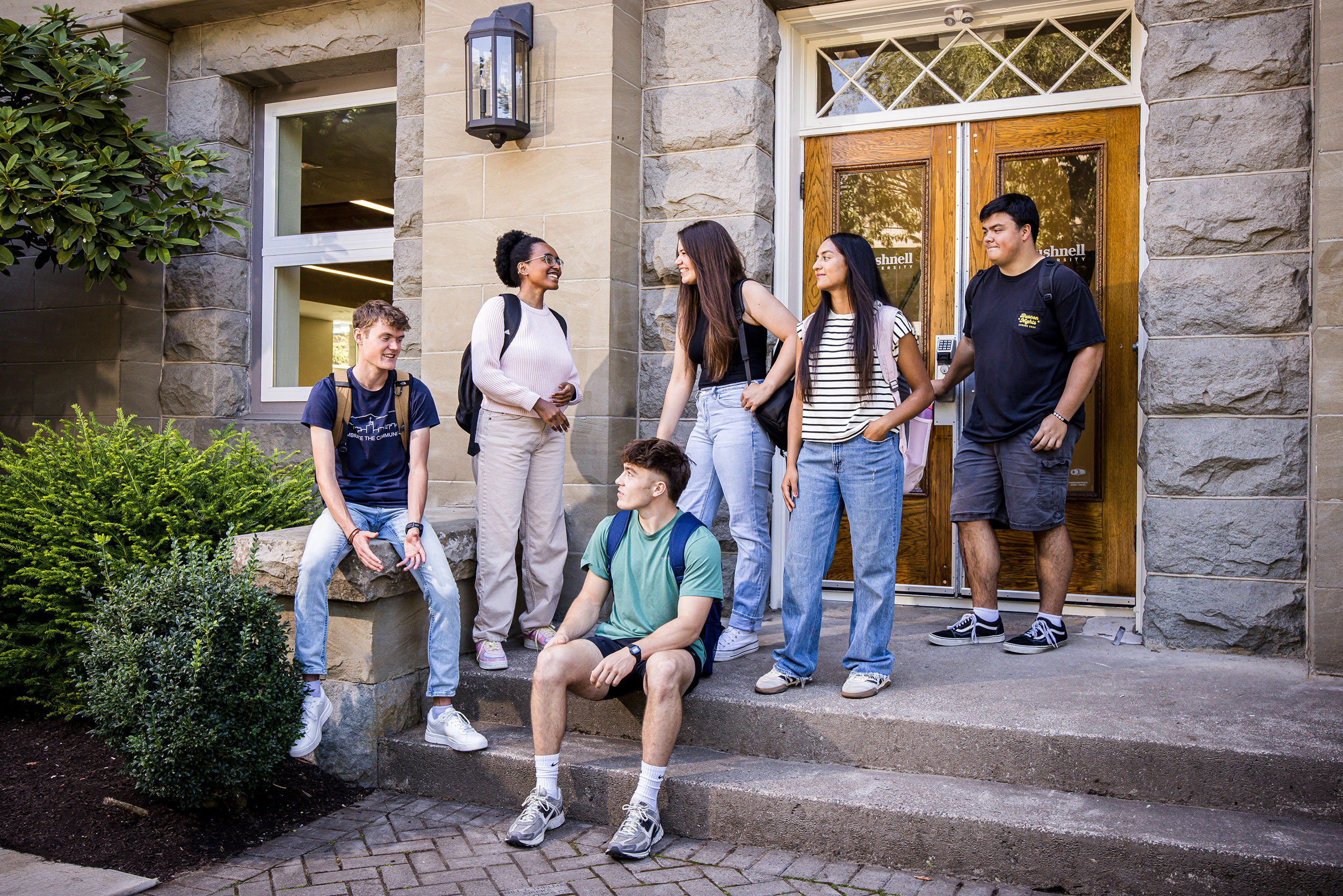 A group of students stand and chat at the stone steps at the front entrance of Goodrich Hall.