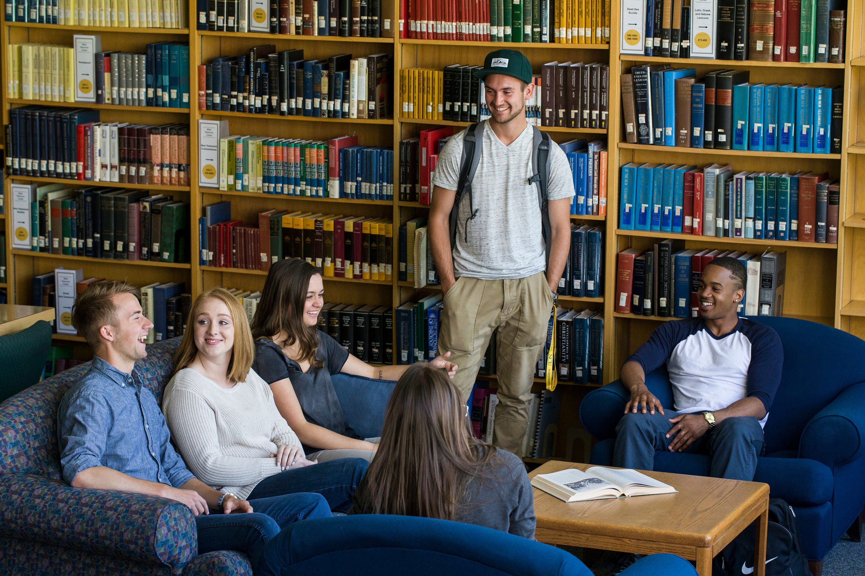 A group of students relax on couches in the campus library with bookshelves behind them.
