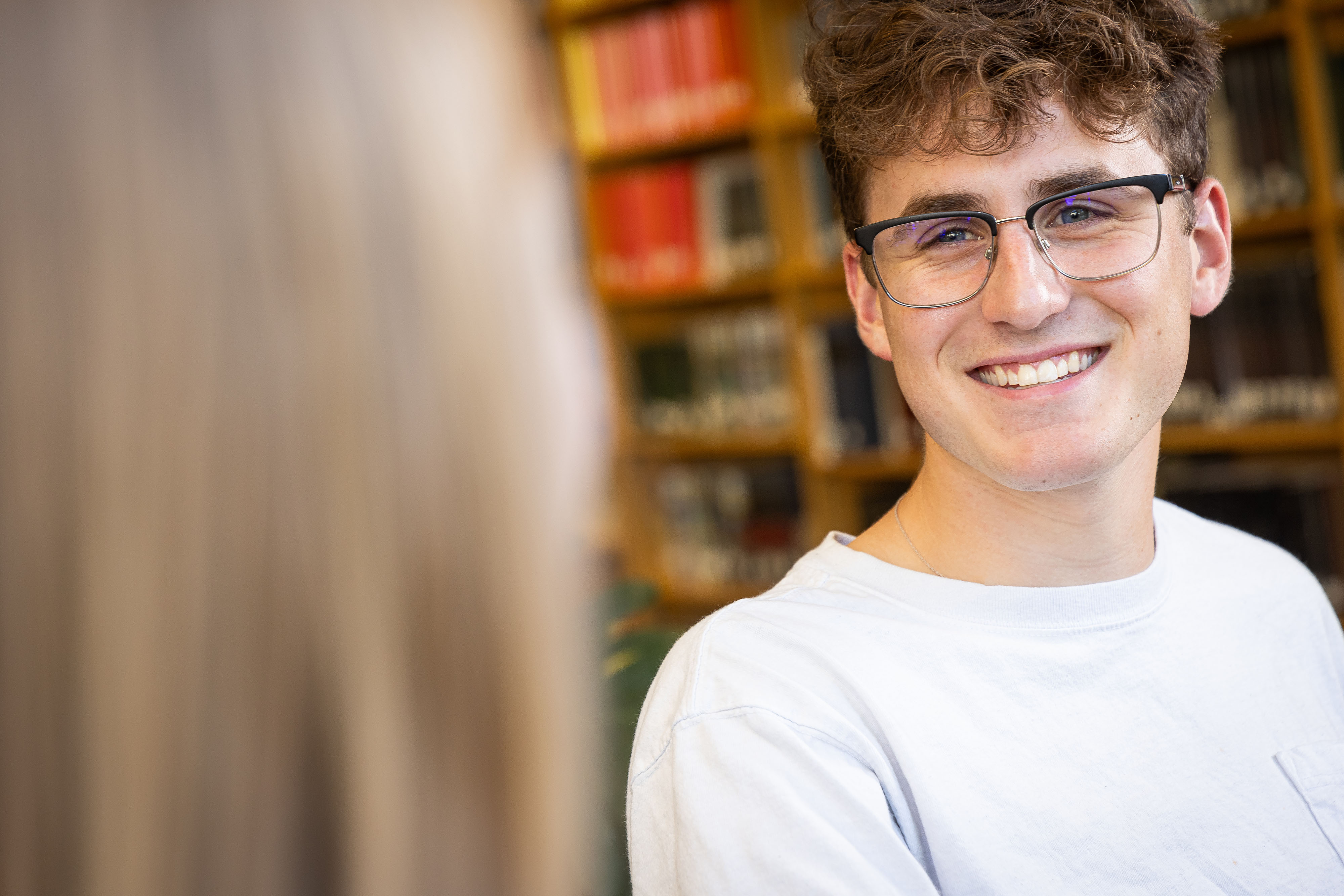 Close up photo of a student with glasses and curly hair face while smiling.