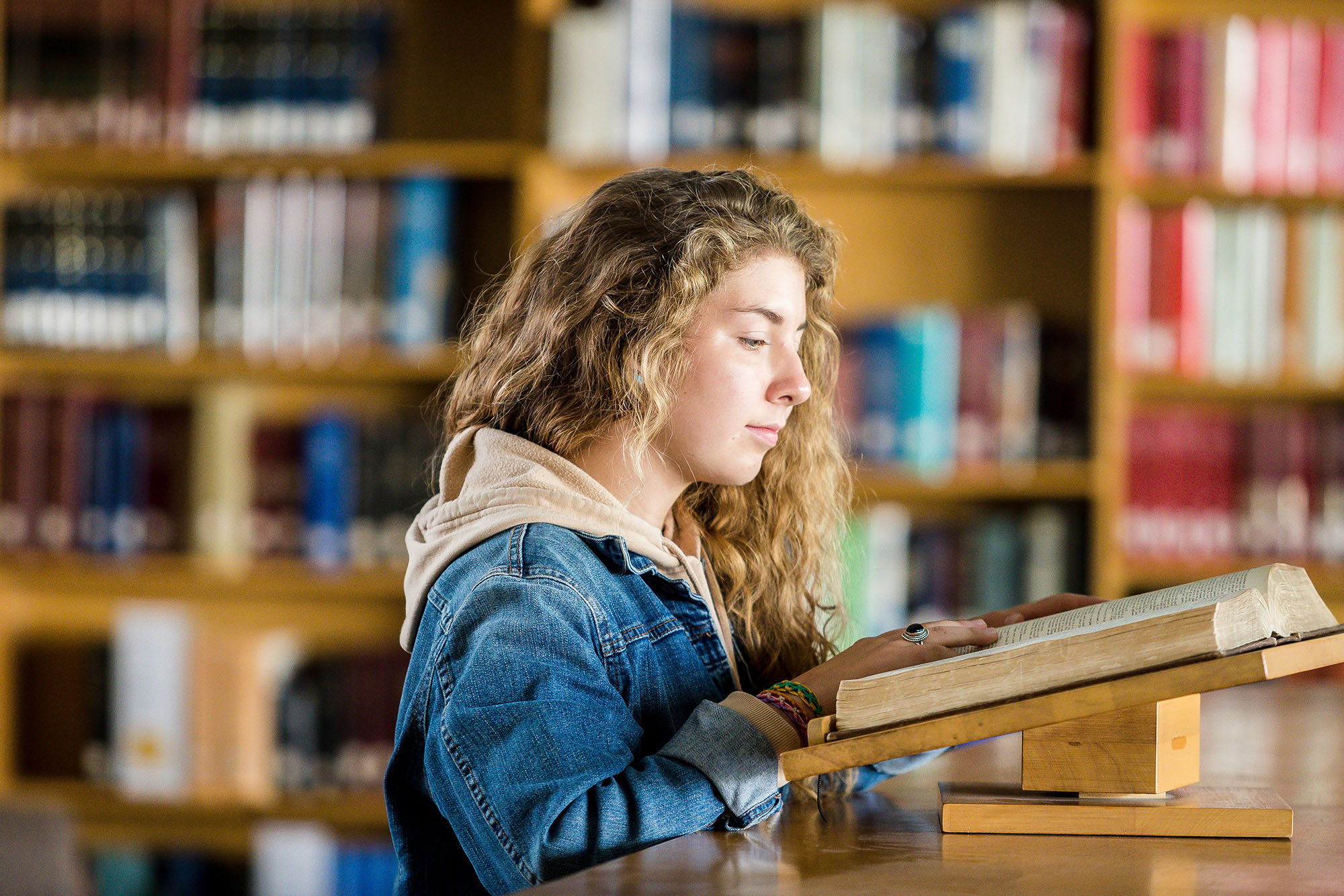 A young student reads a religious book in a library setting.